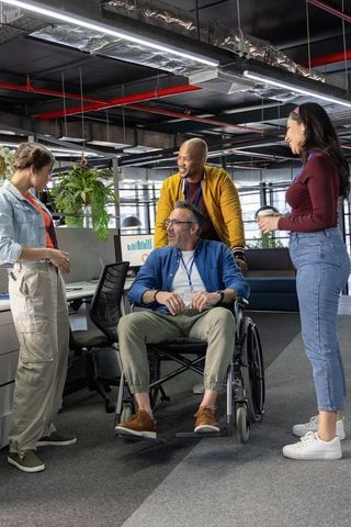 Inclusive office team collaborating with wheelchair colleague over charts in modern workspace