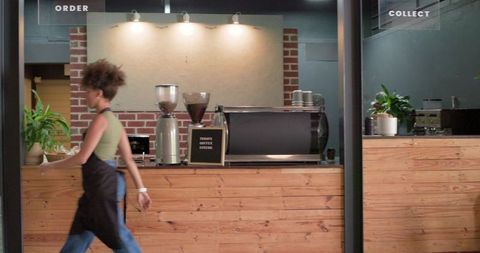Barista walking past rustic wood counter with espresso machine and brick cafe interior