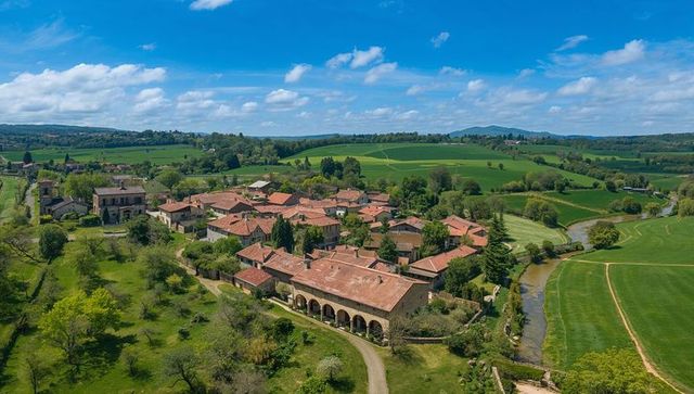 Aerial village in rolling green valley with terracotta roofs, arched arcade and winding creek