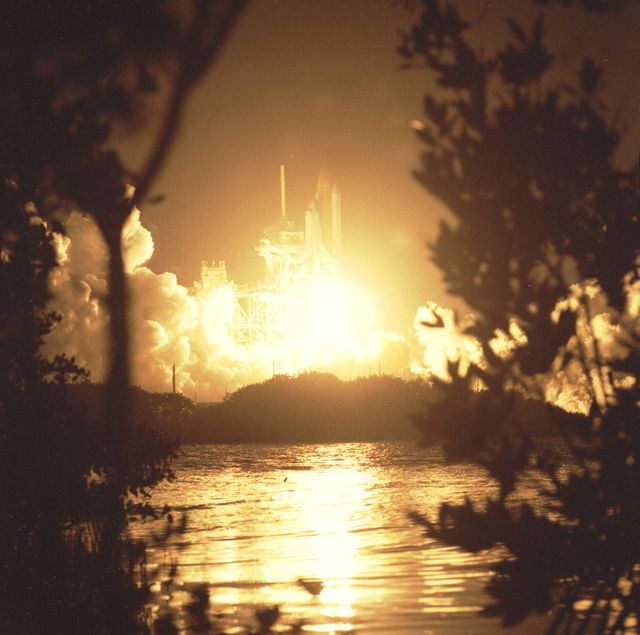 Space Shuttle Endeavour launches at night from Launch Pad 39A on January 22, 1998, framed by silhouettes of Florida foliage. This launch is for STS-89, the eighth docking mission with space station Mir. Useful for studies on space missions, research on NASA endeavors, and space exploration history.
