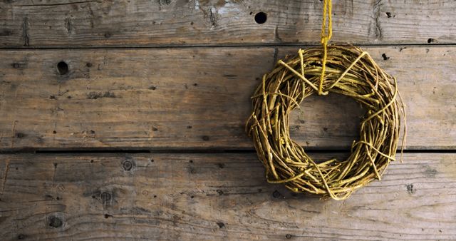 A simple, rustic wreath hangs against a textured wooden background, with copy space. Its minimalist design suggests a natural, country-inspired aesthetic, ideal for seasonal or holiday-themed decor.