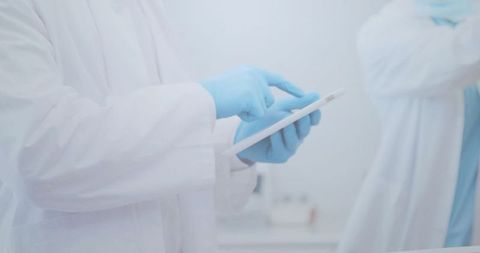 Clinician tapping tablet while wearing blue nitrile gloves in modern medical lab