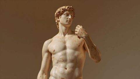 Marble classical sculpture of male torso gazing upward under warm museum gallery light