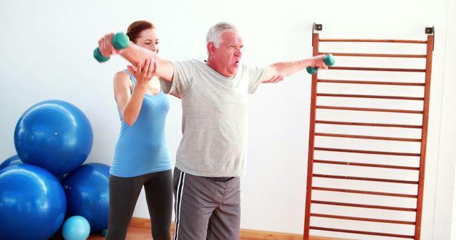 Senior man lifting dumbbells with help from personal trainer in gym poses for physical fitness, rehabilitation, and healthy lifestyle concept. Ideal for use in health and fitness articles, senior well-being promotions, and personal training advertisements.