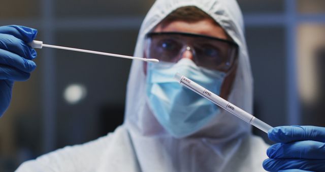 Caucasian male medical worker wearing protective clothing mask and gloves inspecting dna swab in lab. healthcare, medical research technology and hygiene during coronavirus covid 19 pandemic.