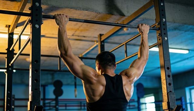 Muscular man performing pull-up on industrial rig showing sculpted back and strength