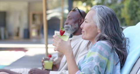 Mature couple relaxing on poolside loungers sipping lemon cocktails with strawberry garnish