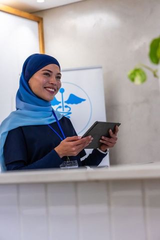Smiling african american healthcare receptionist wearing blue hijab holding tablet