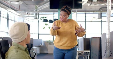 African american woman addressing colleague in open-plan office showing workplace conflict