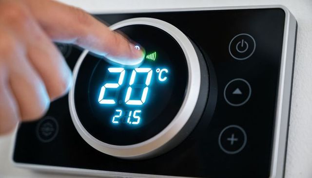 Adjusting smart thermostat dial to 20°c with glowing blue led display, metal ring and wi-fi