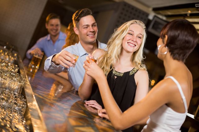 Group of friends enjoying a night out at a bar, toasting with tequila shots. Perfect for themes related to nightlife, social gatherings, celebrations, and friendship. Ideal for use in advertisements, social media posts, and articles about nightlife and social events.
