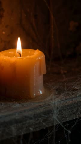 Melting beeswax candle dripping wax on rustic shelf with spiderwebs vertical moody candlelight video