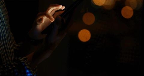 Man Using Smartphone in Dim Lighting with Amber Bokeh