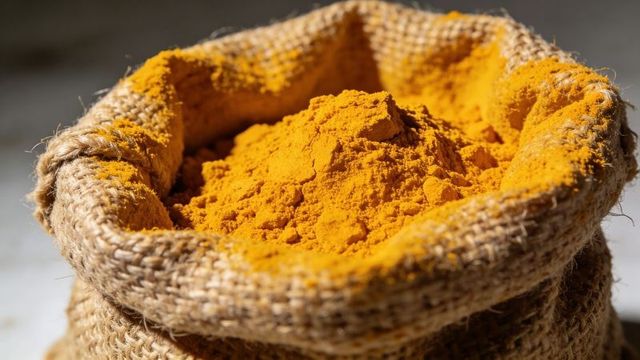 Displaying golden turmeric powder in rustic jute sack closeup for cooking and wellness