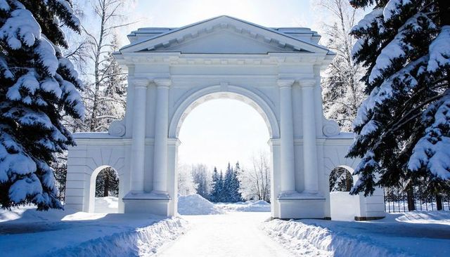 Neoclassical triumphal arch gateway in snowy park framing cleared winter path
