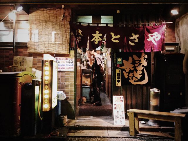 Traditional Japanese izakaya displayed at night with brightly glowing yellow lanterns, wooden signage, and welcoming entryway. Suitable for themes involving Japanese culture, night scenes, urban exploration, street photography, Asian cuisine, and traditional settings.