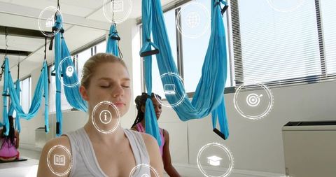 Meditating woman practicing aerial yoga with hammocks and wellness icons in sunlit studio