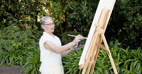 Senior Woman Painting on Canvas in Tranquil Garden Setting