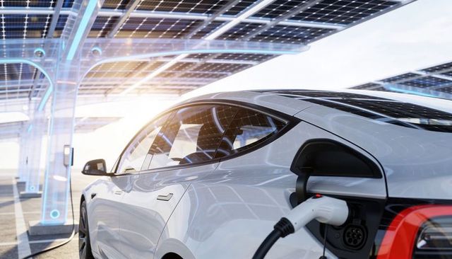 White electric sedan charging under solar canopy at ev station with sunlight reflections