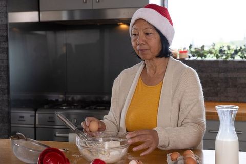 Senior woman preparing holiday dough with santa hat and kitchen utensils