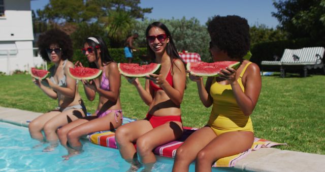 A vibrant poolside scene with four women of diverse backgrounds sitting on the edge of a swimming pool, enjoying large slices of watermelon. They are in colorful swimwear, laughing and having fun under the bright sun. Ideal for use in ads, social media, or articles about summer activities, healthy eating, friendships, and leisure time.