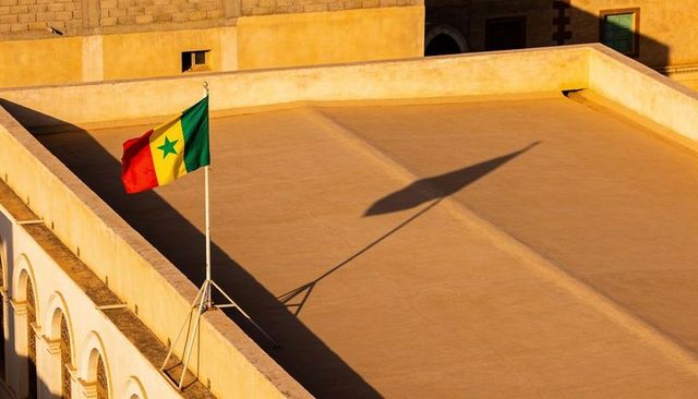 Senegal flag flying over sunlit rooftop at golden hour casting dramatic long shadow
