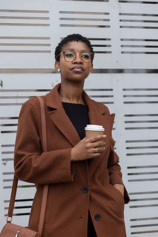 Confident african american woman standing with coffee in brown coat urban portrait