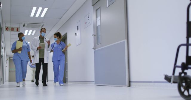 Healthcare professionals walking down a hospital corridor in protective masks and discussing patient records. Ideal for illustrating teamwork in healthcare settings, advertisements for medical services, or educational materials on hospital procedures.