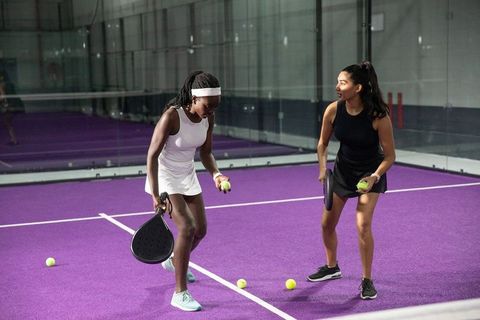 Women practicing paddle drills on purple indoor court holding paddles and yellow balls