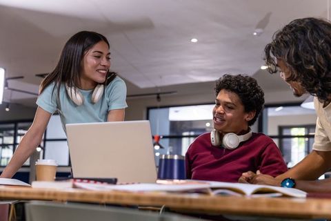 Diverse college students collaborating around laptop in modern coworking study space