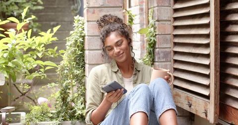 Woman Relaxing in Garden with Smartphone and Coffee