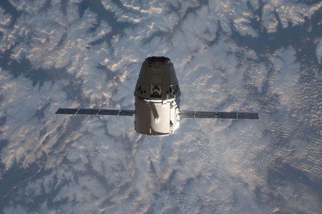 Depicts SpaceX Dragon cargo craft approaching International Space Station for docking using Canadarm2 robotic arm. First commercially developed ASV to join ISS. Useful for topics on space exploration, technology, commercial spaceflight, NASA missions, and space station logistics.