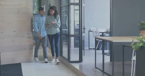 Young coworkers walking and checking smartphone while collaborating in modern glass office