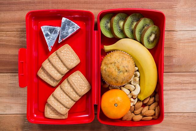 Various snack and fruit in lunch box on wooden table