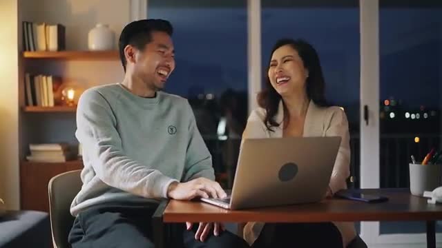 Happy Couple Laughing While Using Laptop at Night
