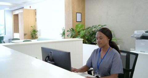Medical receptionist wearing scrubs and blue lanyard checking monitor in clinic