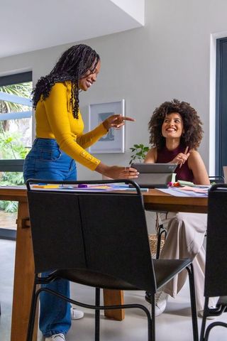 African american women collaborating in bright home office, brainstorming on tablet