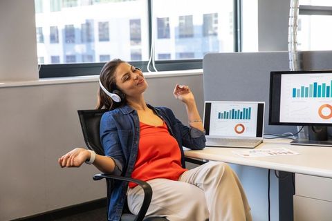 Office woman reclining with headphones enjoying break while reviewing business charts