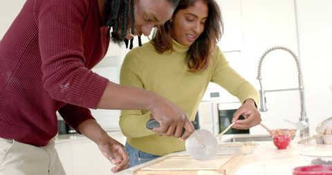 Diverse couple baking together cutting pastry dough with wheel cutter on kitchen island