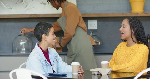 Friends chatting over takeaway coffee in modern minimalist cafe with smiling barista