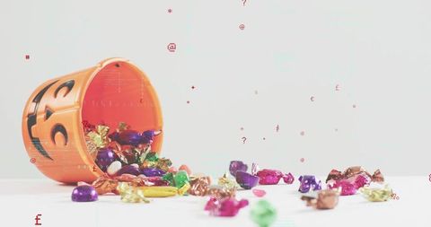 Orange jack-o'-lantern bucket spilling colorful foil candies on white surface