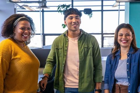 Diverse team smiling and collaborating in bright modern open-plan office with plants, natural light