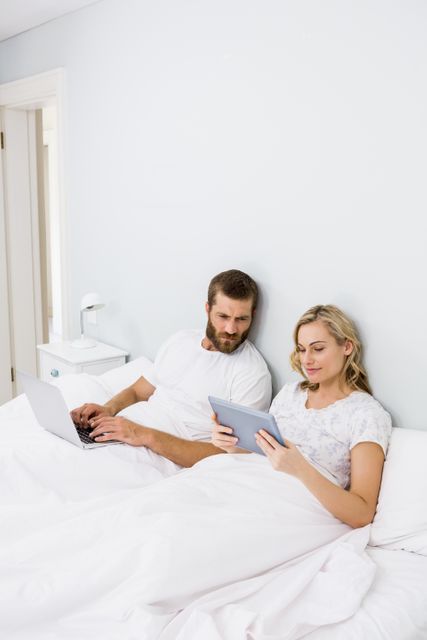 Couple using laptop and digital tablet in bed at bedroom