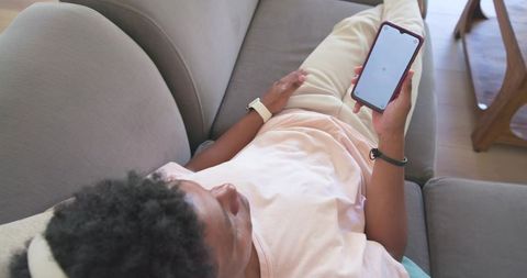 Relaxing african american man reclining on sofa checking smartphone during home downtime