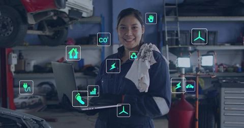 Woman mechanic monitoring ev diagnostics and sustainability metrics on laptop in workshop