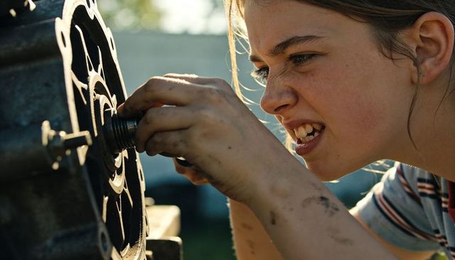 Teenage girl repairing engine part outdoors tightening bolt with focused determination
