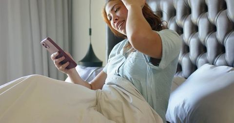 Woman checking smartphone in bed smiling at notification with icons overlay and cozy mood