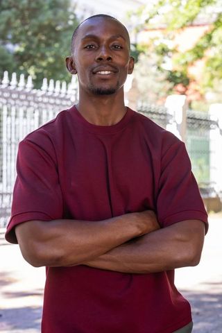 Confident african american man standing with arms crossed in maroon shirt, sunlit portrait