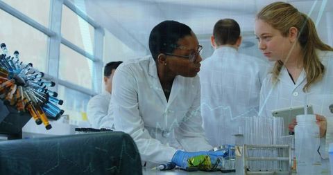 Female scientists collaborating at lab bench discussing data with tablet and rotor