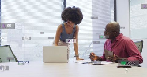 Collaborative mentorship moment woman leaning over laptop engaging colleague in conference room